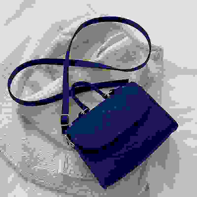 Navy blue small square single shoulder bag with crossbody strap, displayed on a soft textured surface for detail emphasis.