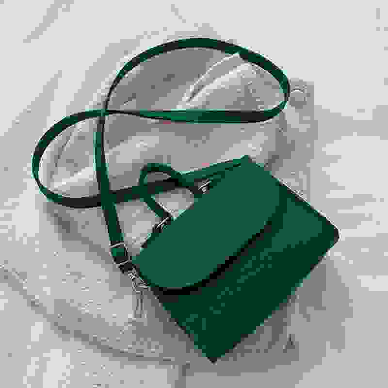 Dark green small square crossbody bag with top handle and adjustable strap, designed for stylish everyday use.