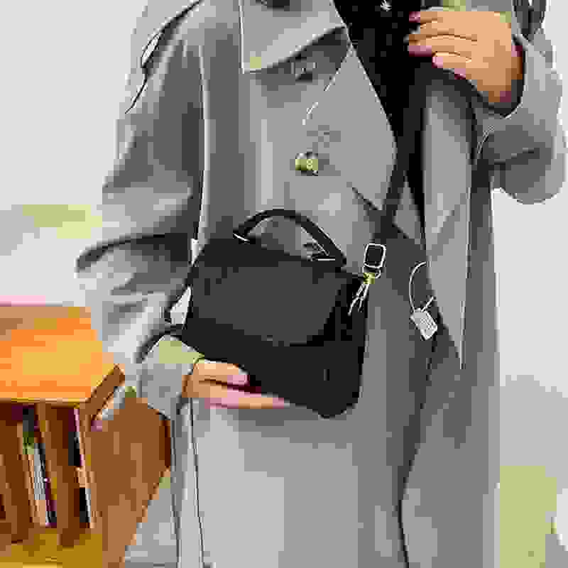 Woman wearing a gray coat holding a black leather small square crossbody bag, showcasing its compact and stylish design.