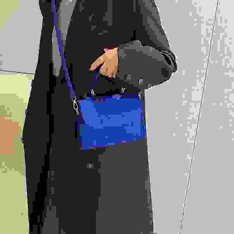 Bright blue small square single shoulder bag worn crossbody style, adding a pop of color to a neutral outfit.